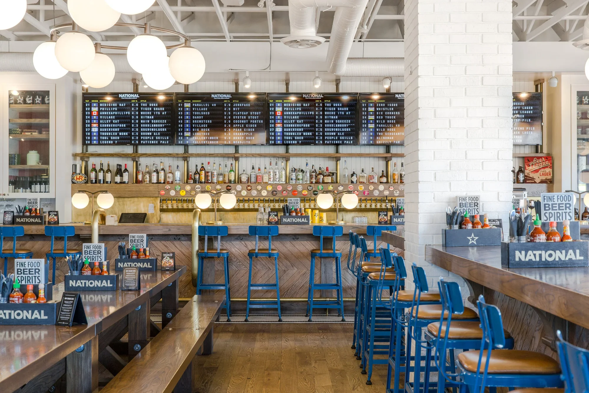Restaurant interior with digital tap-list boards, a bar, and blue seating